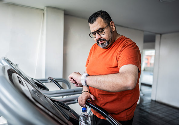 A middle-aged man checks his watch on the treadmill