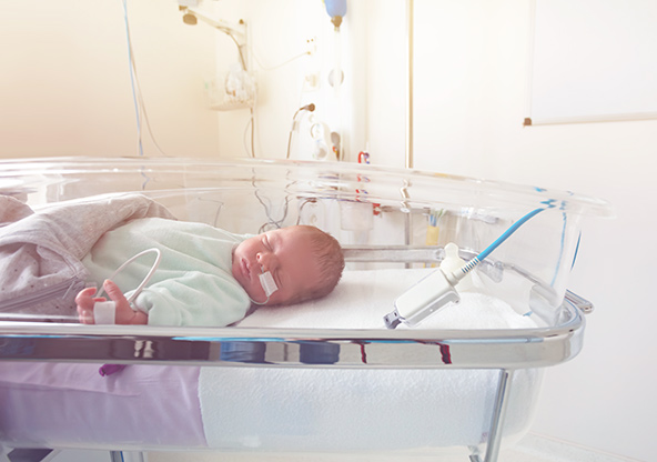 A newborn baby sleeps in the NICU crib