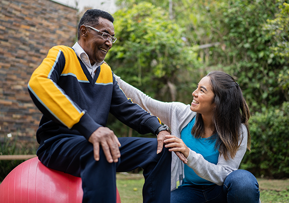 An elderly African-American man sitting on an exercise ball doing cardiac rehabilitation with his therapist